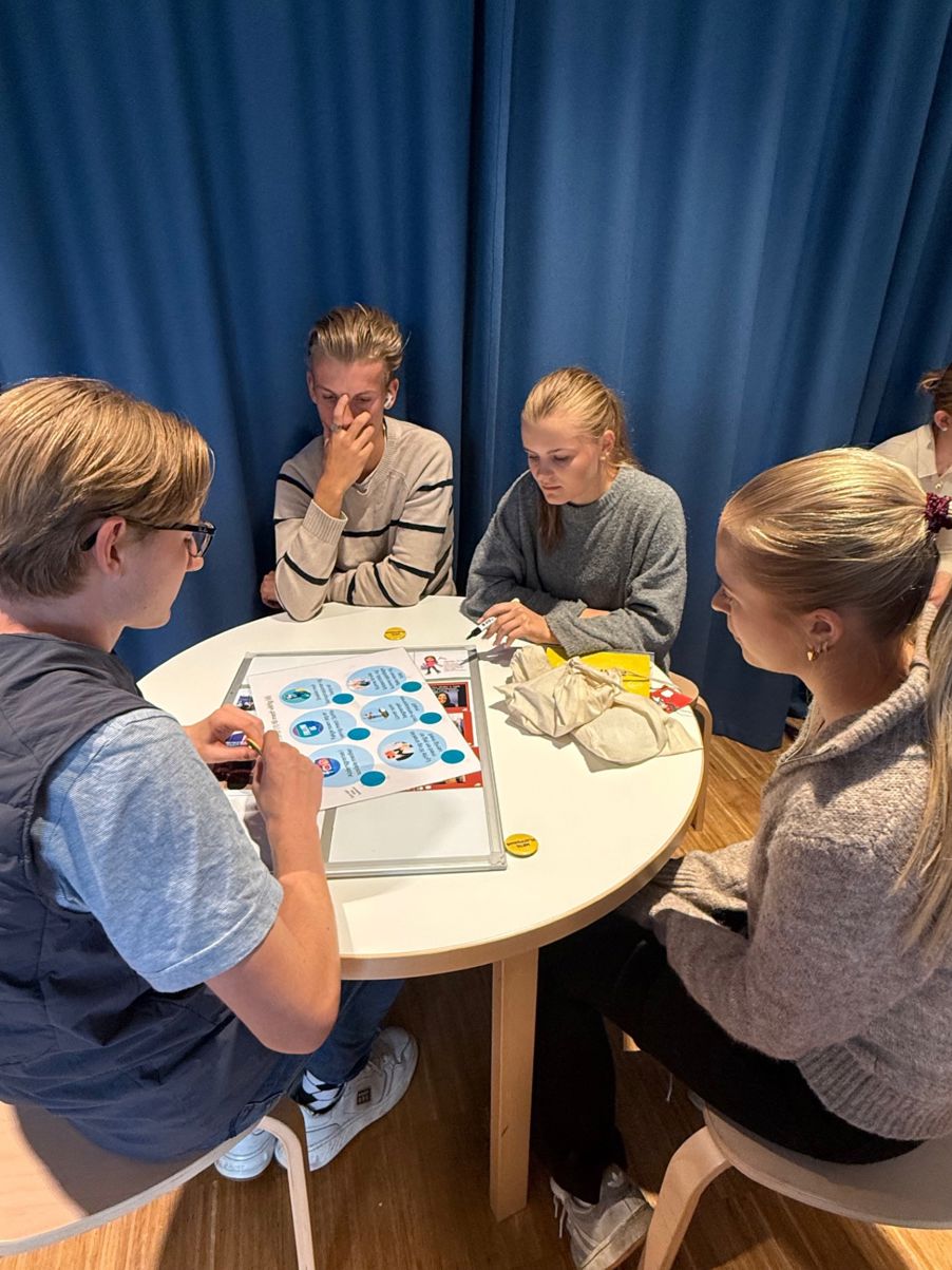 en gruppe mennesker som sitter rundt et bord og spiller et brettspill