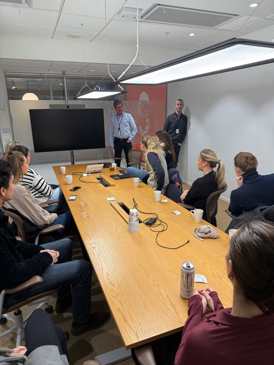 en gruppe mennesker som sitter rundt et bord med en person stående i midten en gruppe mennesker som sitter rundt et bord med en person stående i midten