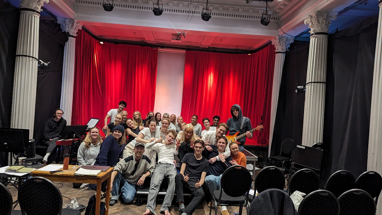 en gruppe mennesker som sitter i et rom med et rødt gardin